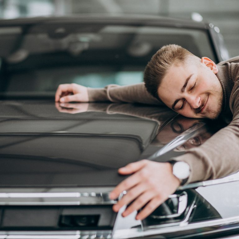 Young handsome man hugging a car in a car showroom